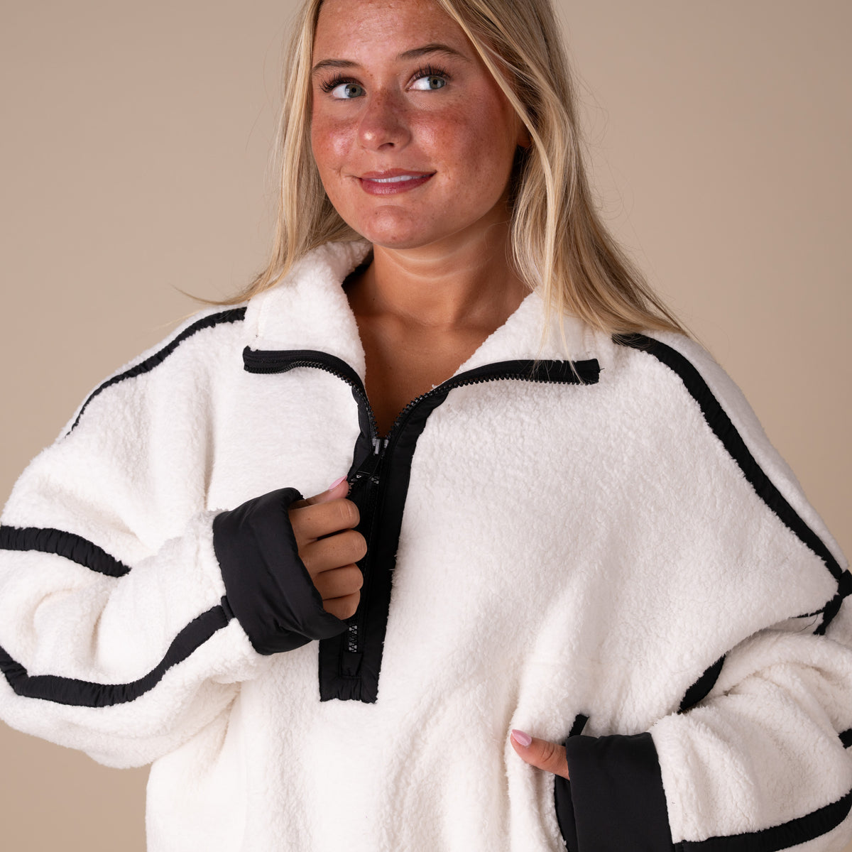 Woman wearing a white and black fleece jacket on a beige background
