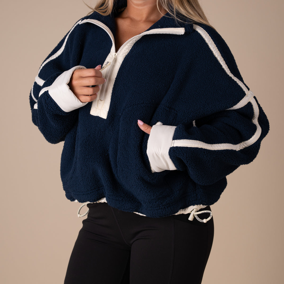Woman wearing a navy and off white fleece jacket on a beige background
