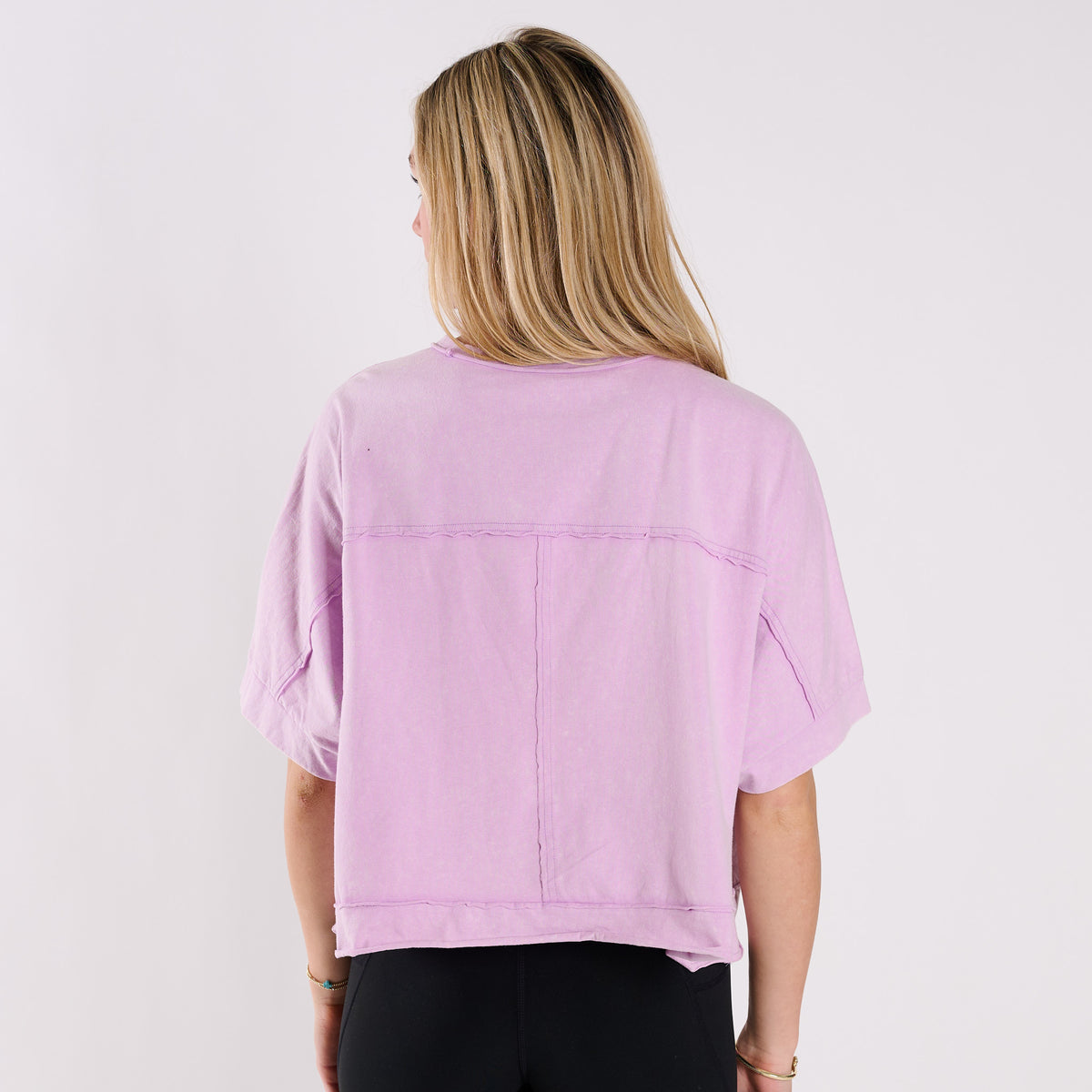 Woman wearing a lavender oversized cropped shirt and black pants on a white background