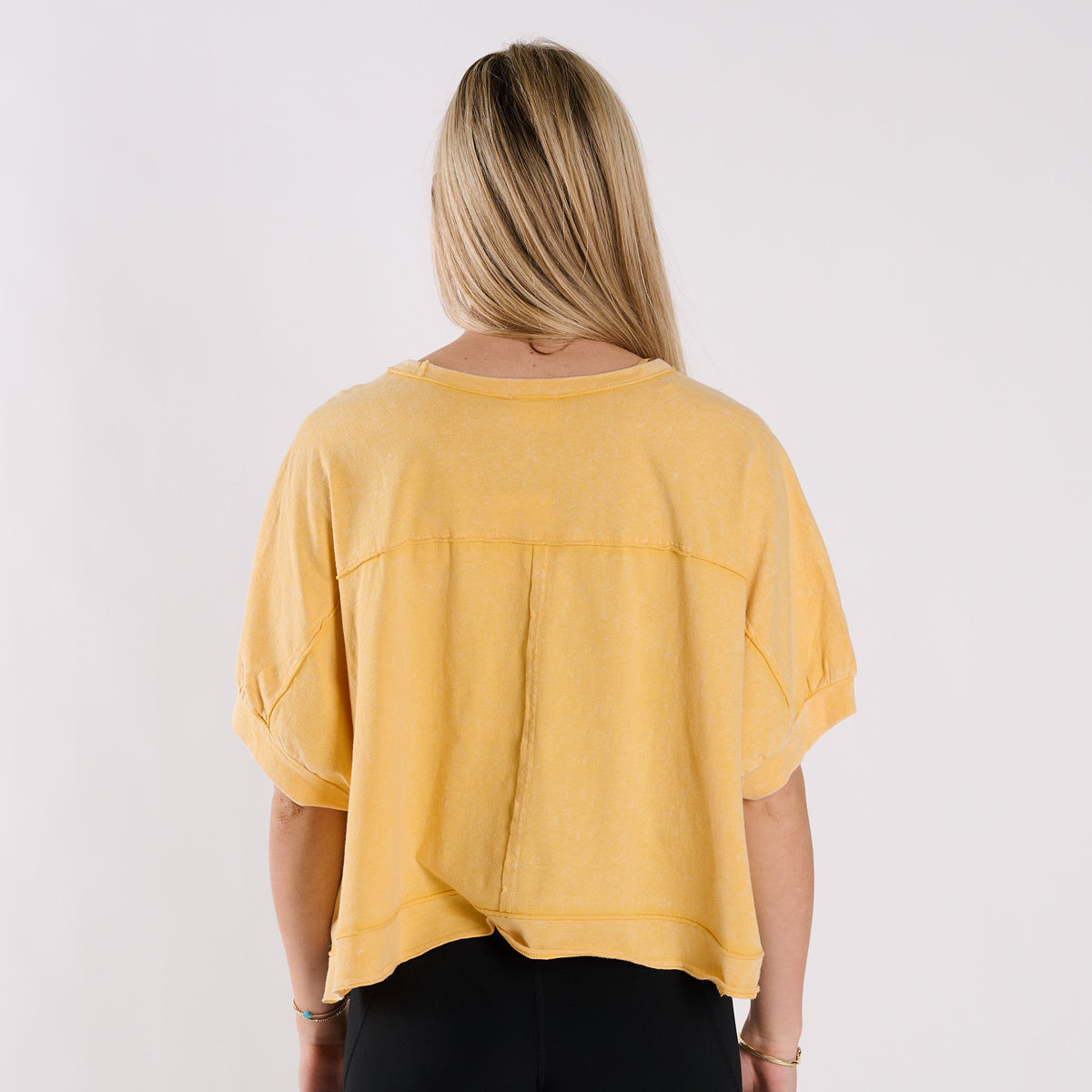 Woman wearing a yellow oversized cropped shirt and black pants on a white background