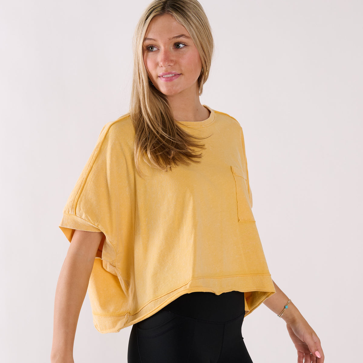 Woman wearing a yellow oversized cropped shirt and black pants on a white background