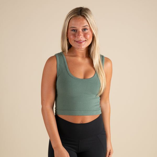  Woman wearing a green tank top and black leggings against a beige background