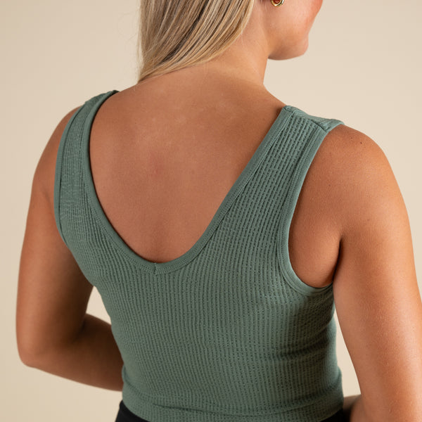  Person wearing a green ribbed tank top on a beige background