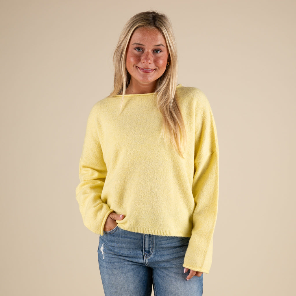 Woman wearing a yellow sweater and blue jeans against a beige background