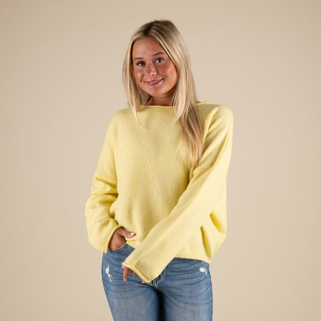 Woman wearing a yellow sweater and blue jeans against a beige background