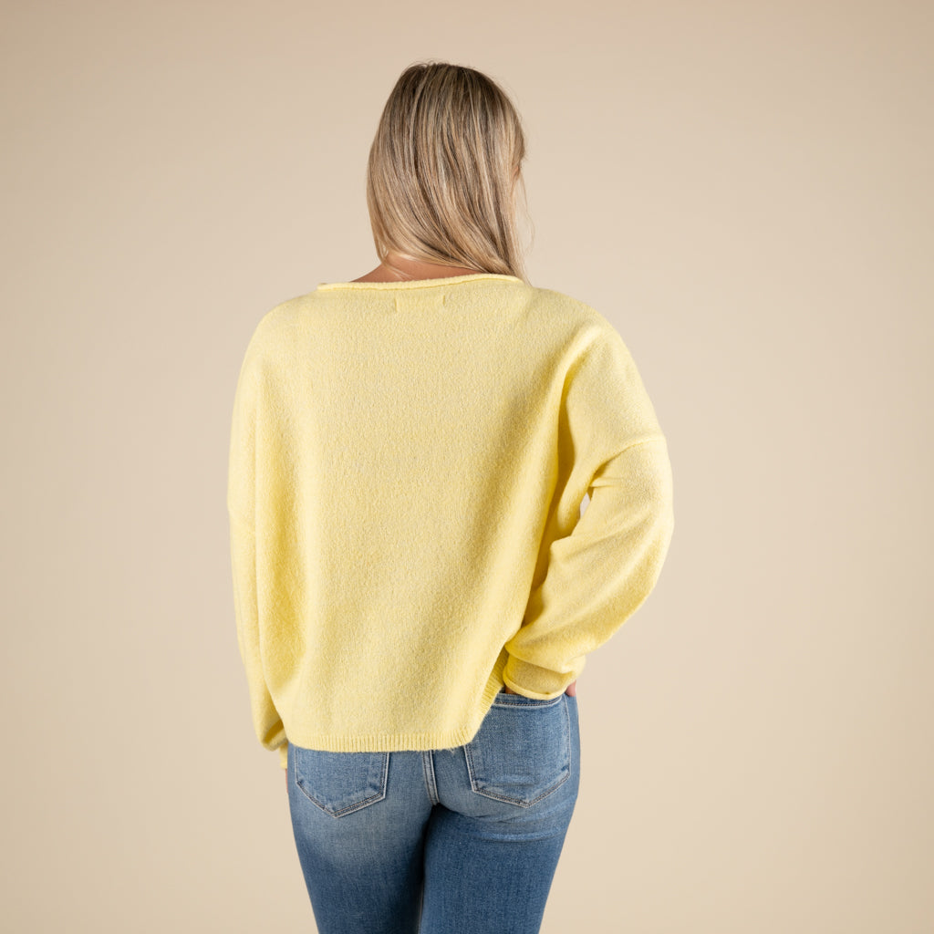 Person wearing a yellow sweater and blue jeans on a beige background
