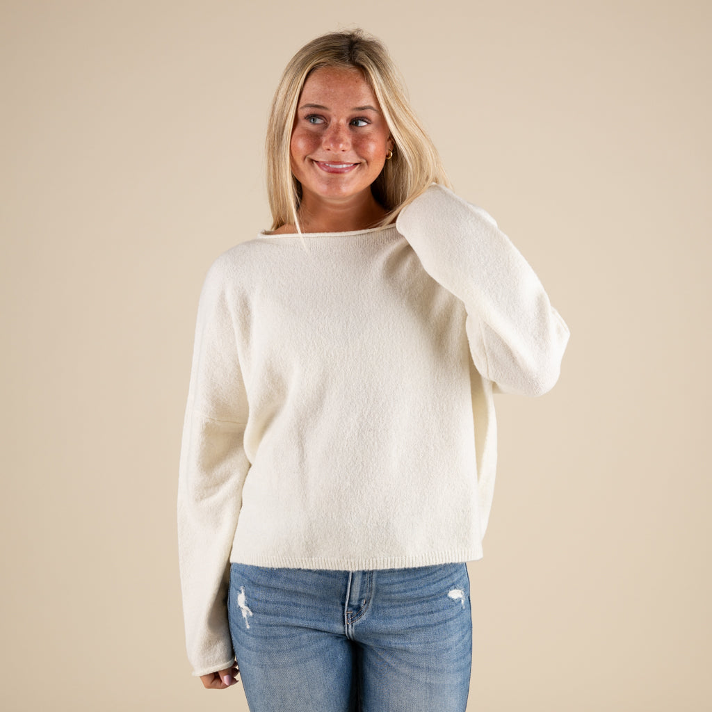 Woman wearing a white sweater and blue jeans against a beige background