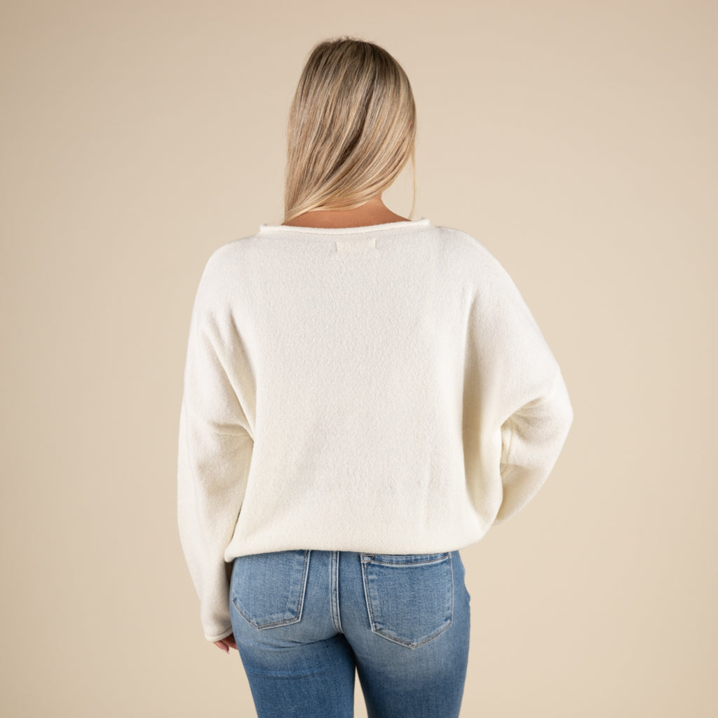 Person wearing a white sweater and blue jeans on a beige background