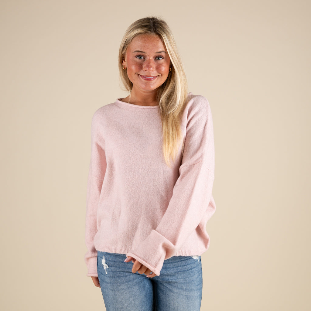 Woman wearing a light pink sweater and blue jeans against a beige background