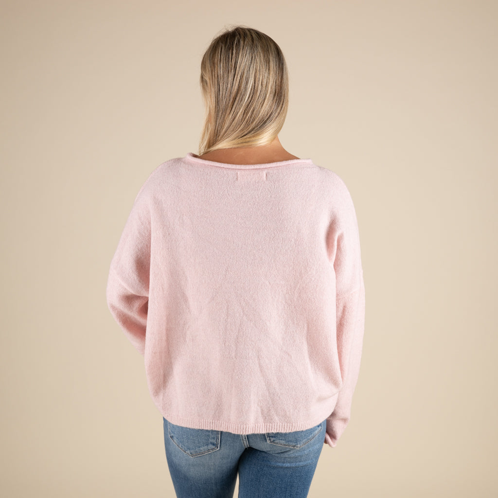 Person wearing a light pink sweater and blue jeans on a beige background