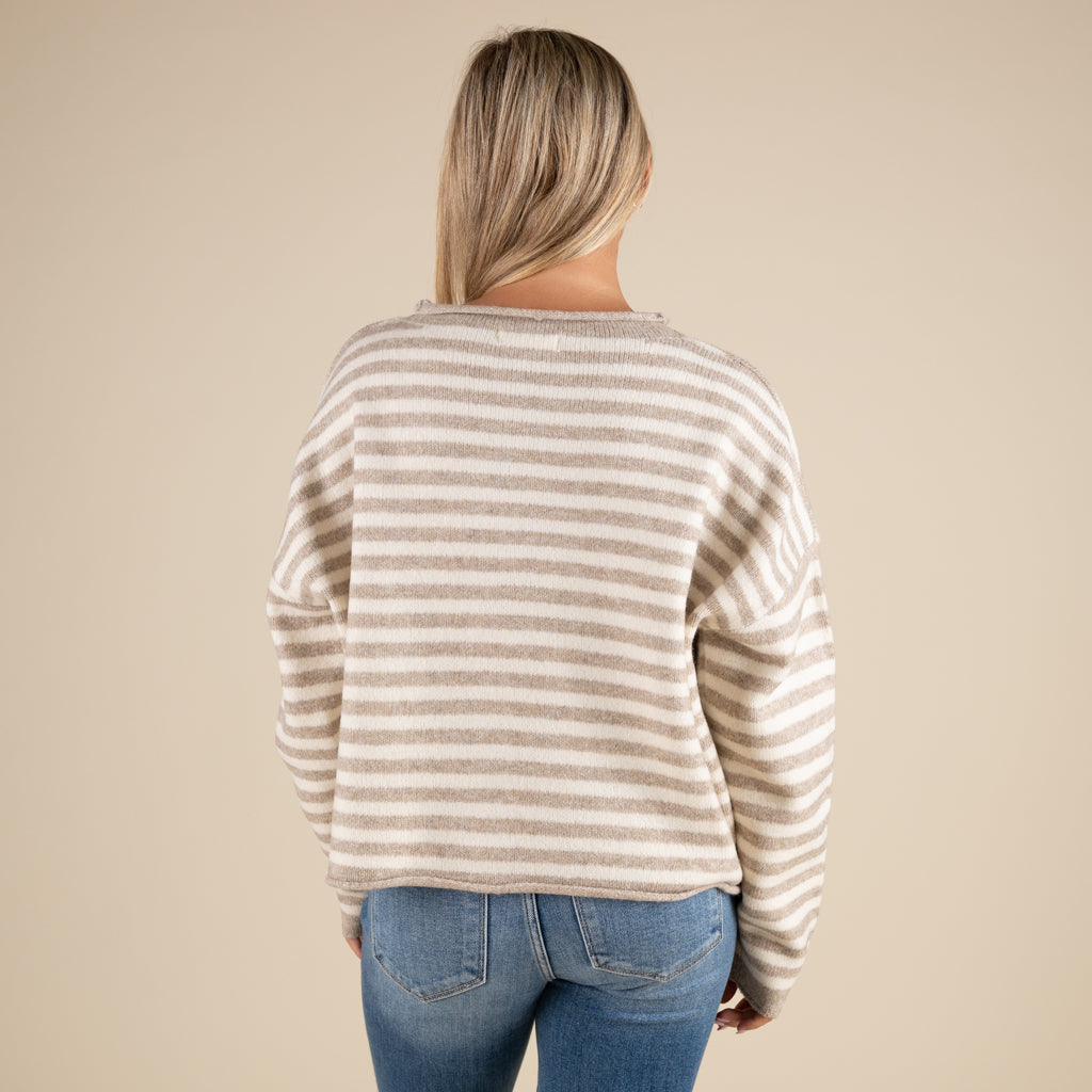 Person wearing a striped sweater and jeans on a beige background