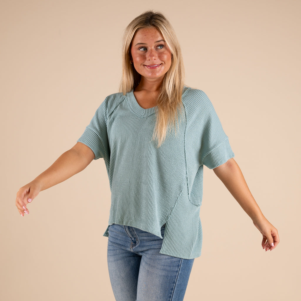 Woman wearing a green ribbed top and blue jeans on a beige background
