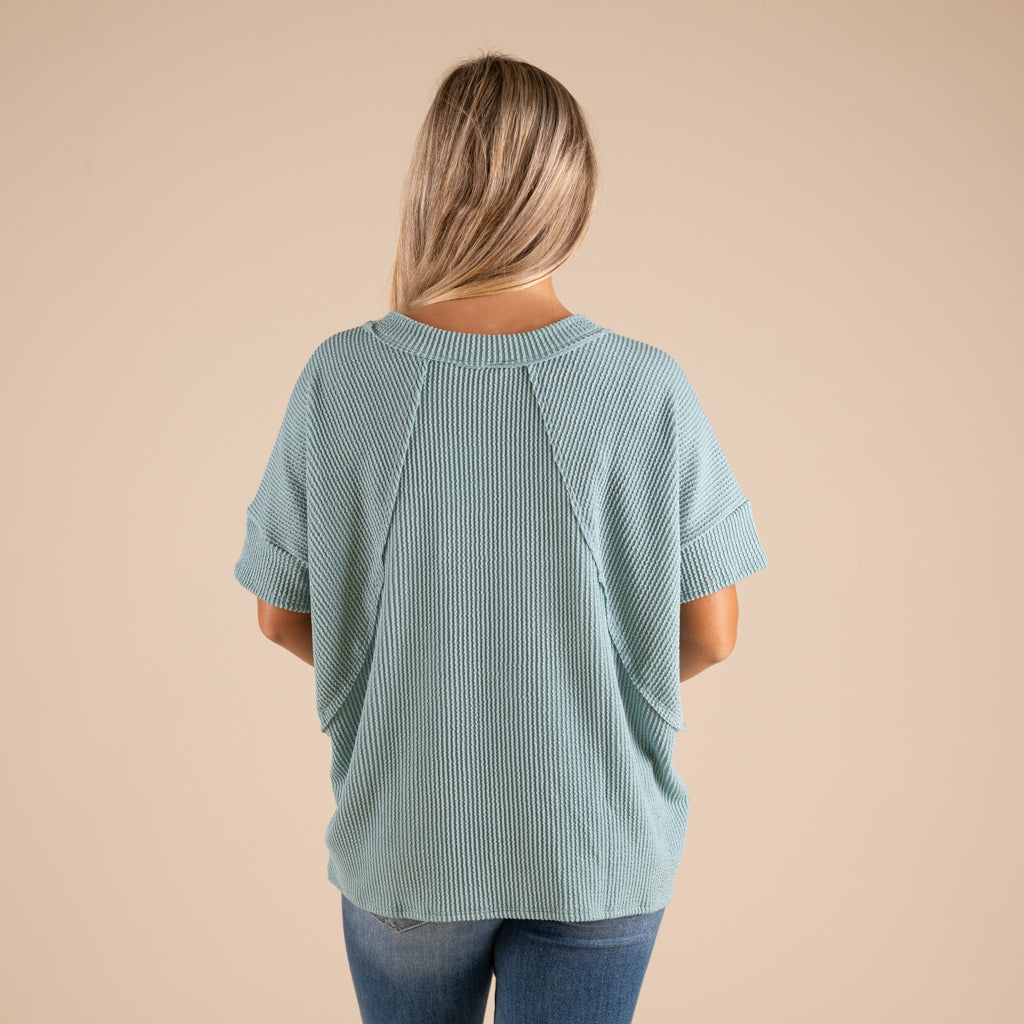 Woman wearing a green ribbed top and blue jeans on a beige background