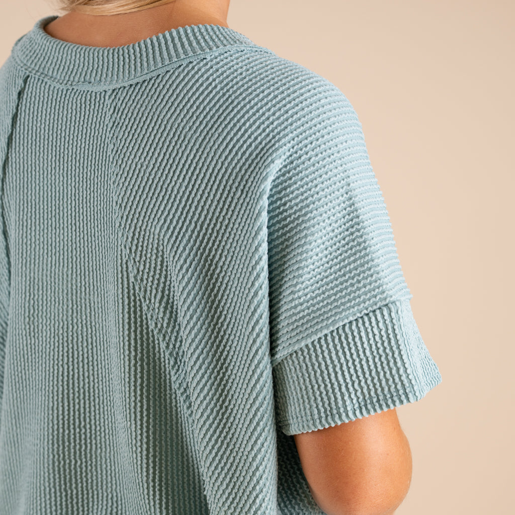 Woman wearing a green ribbed top and blue jeans on a beige background