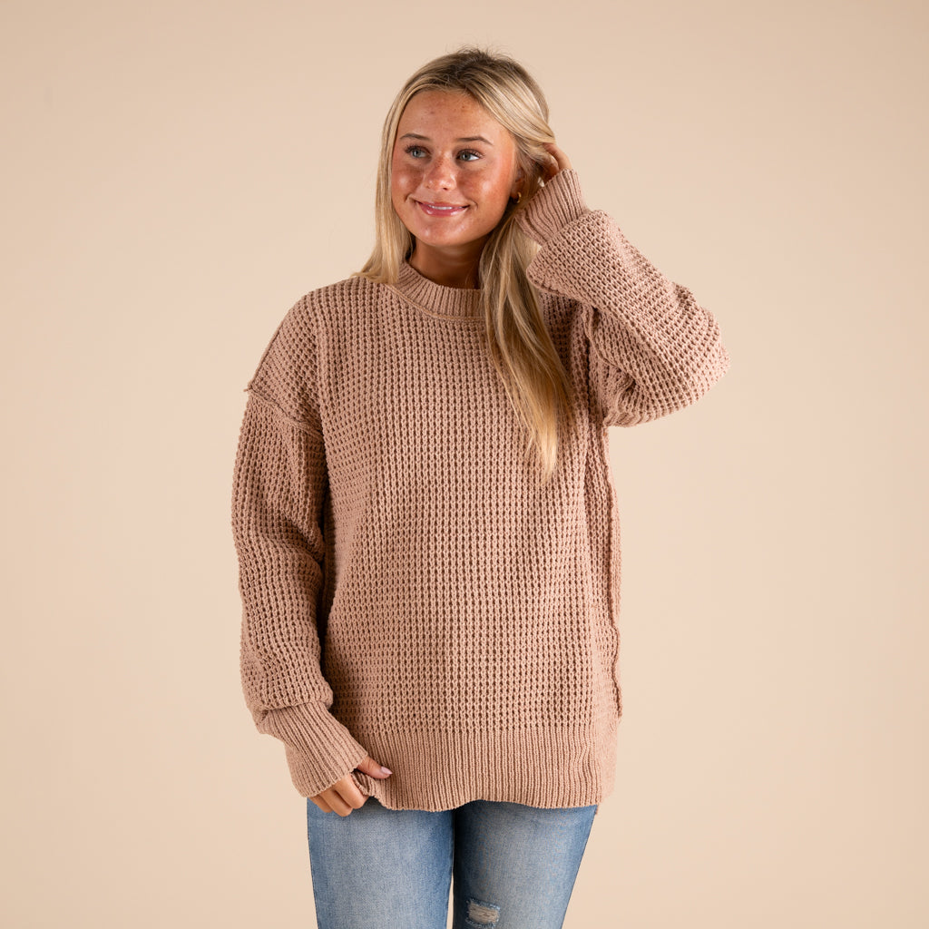 Woman wearing a beige sweater and blue jeans on a beige background