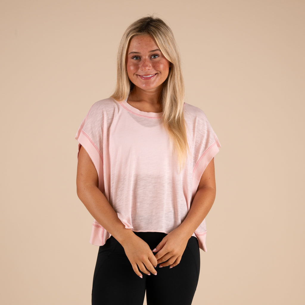 Woman wearing a light pink t-shirt and black pants on a beige background