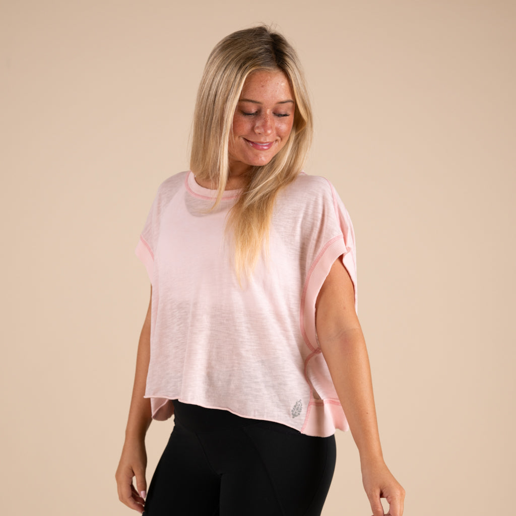 Woman wearing a light pink t-shirt and black leggings on a beige background