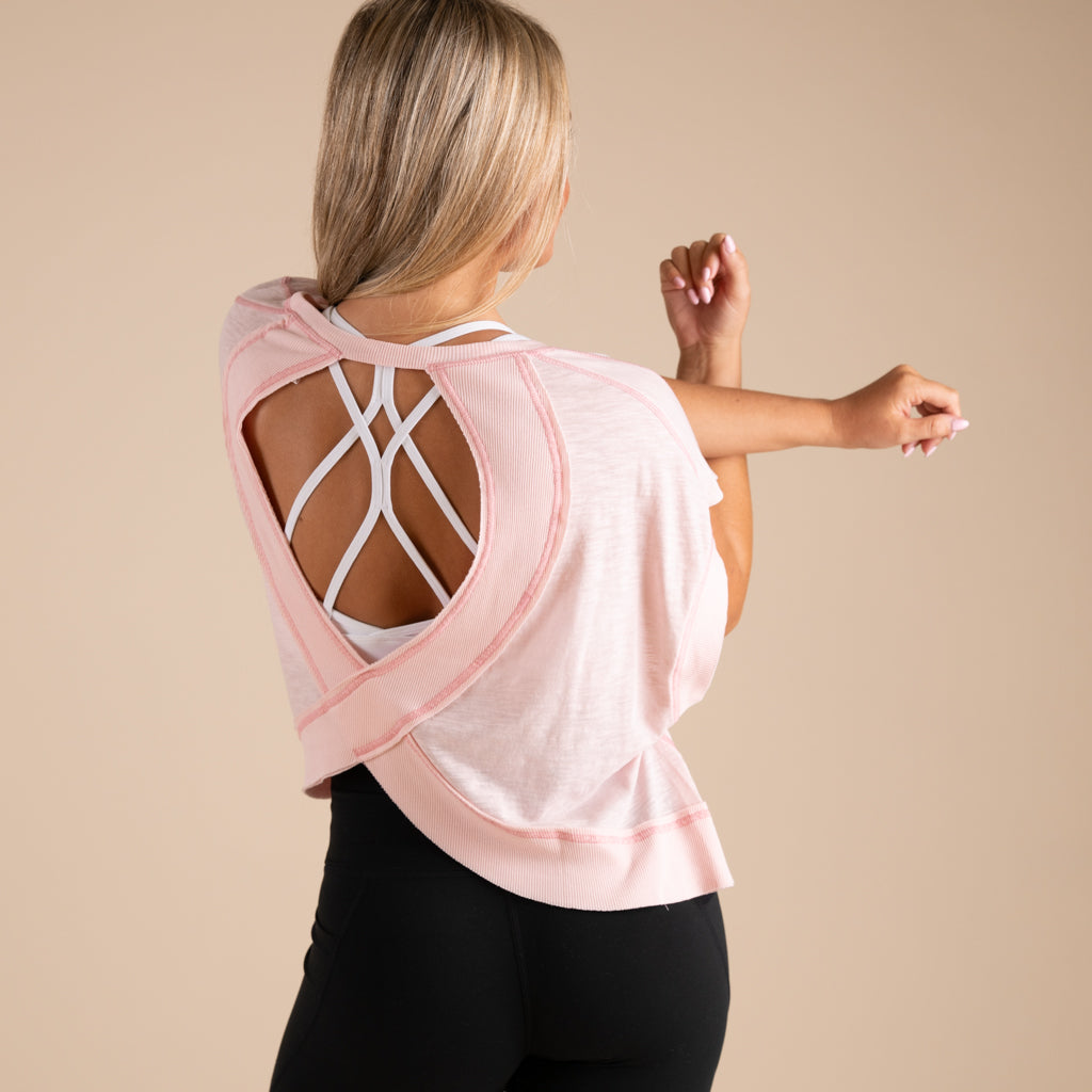 Woman wearing a pink top with cut-out back design on a beige background