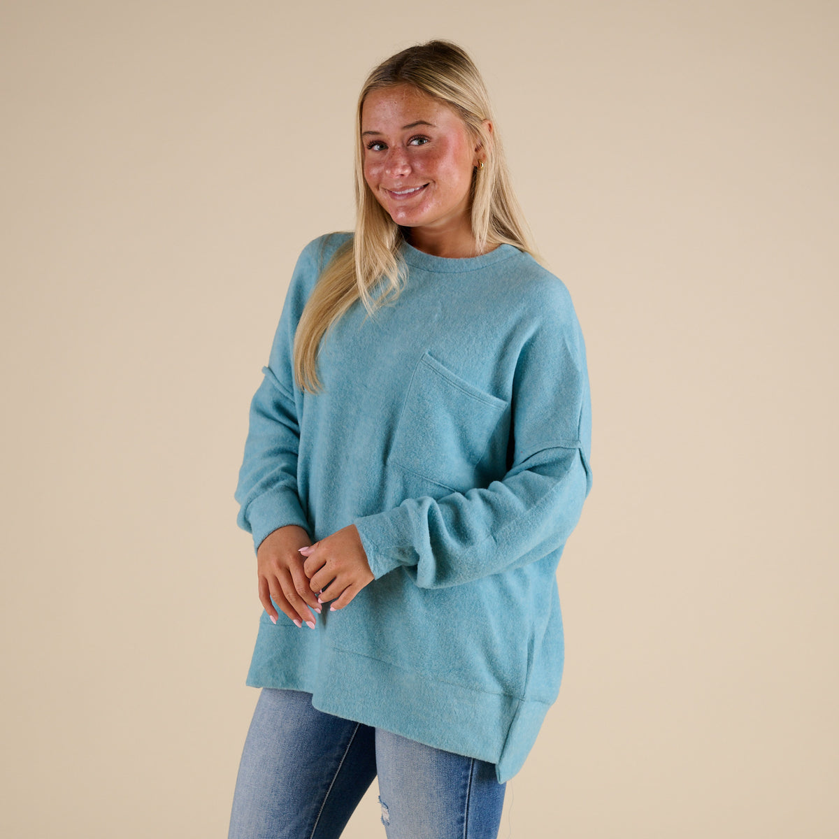 Woman wearing a light blue sweater with a pocket on a beige background