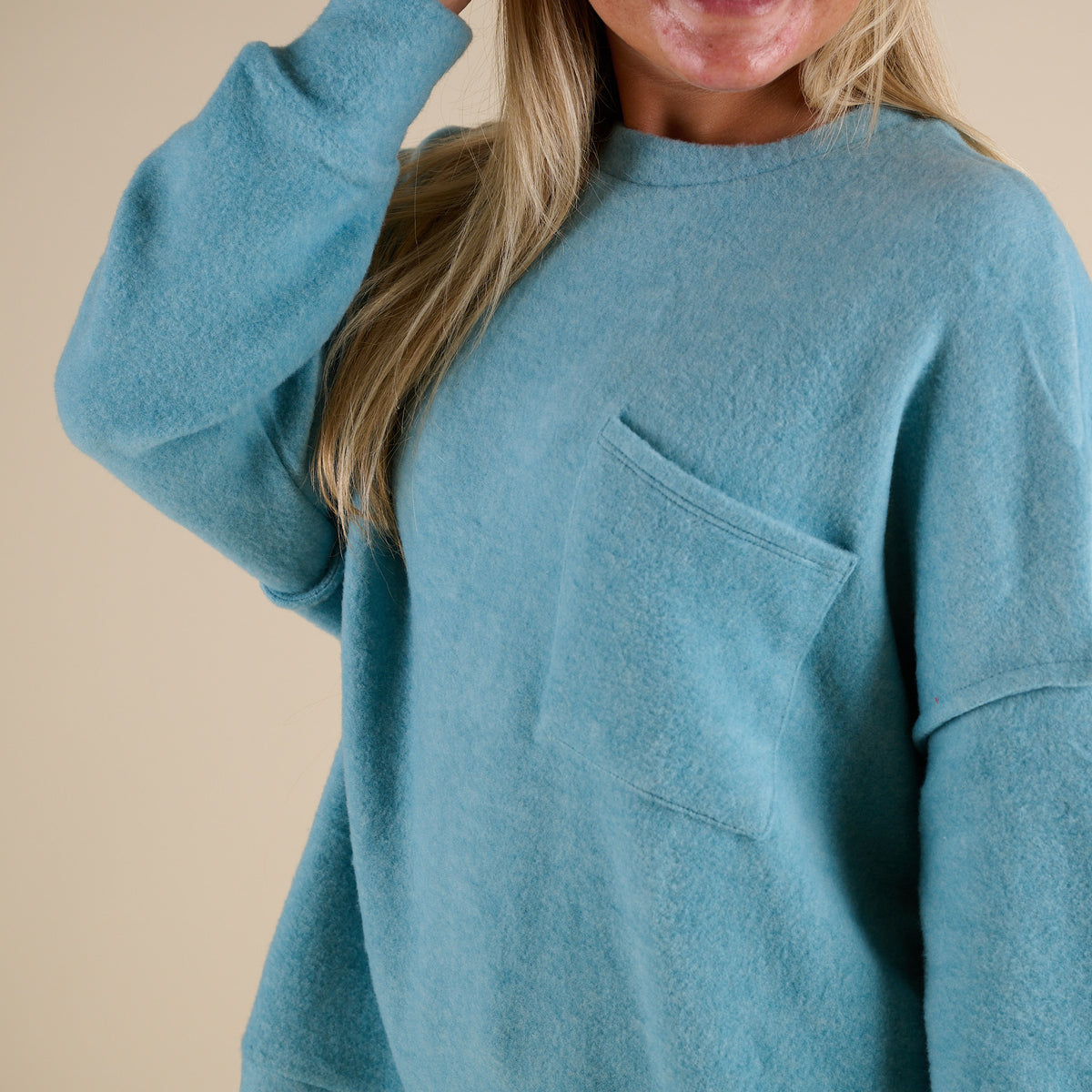 Teal sweatshirt worn by a person on a beige background