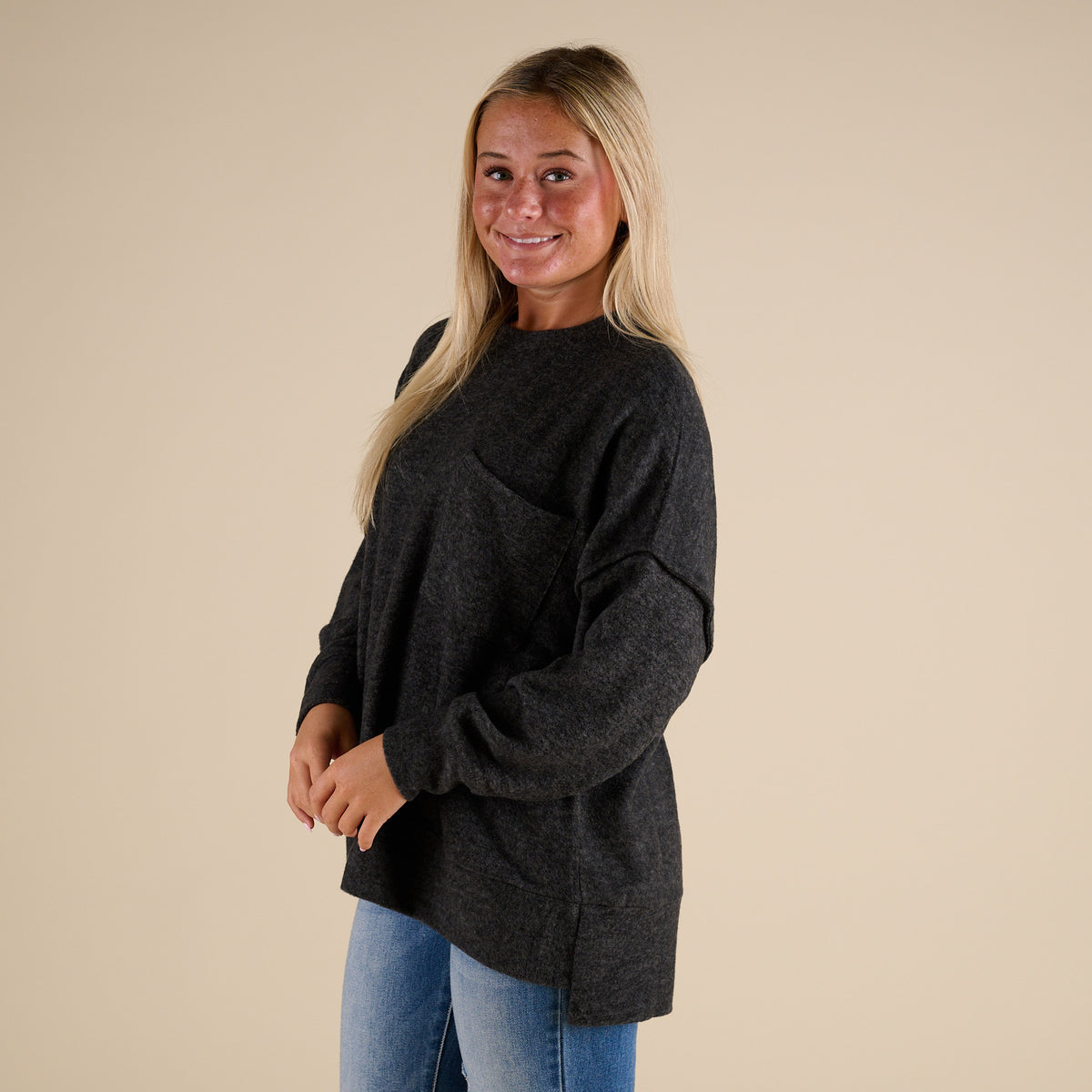 Woman wearing a dark gray sweater and blue jeans against a beige background