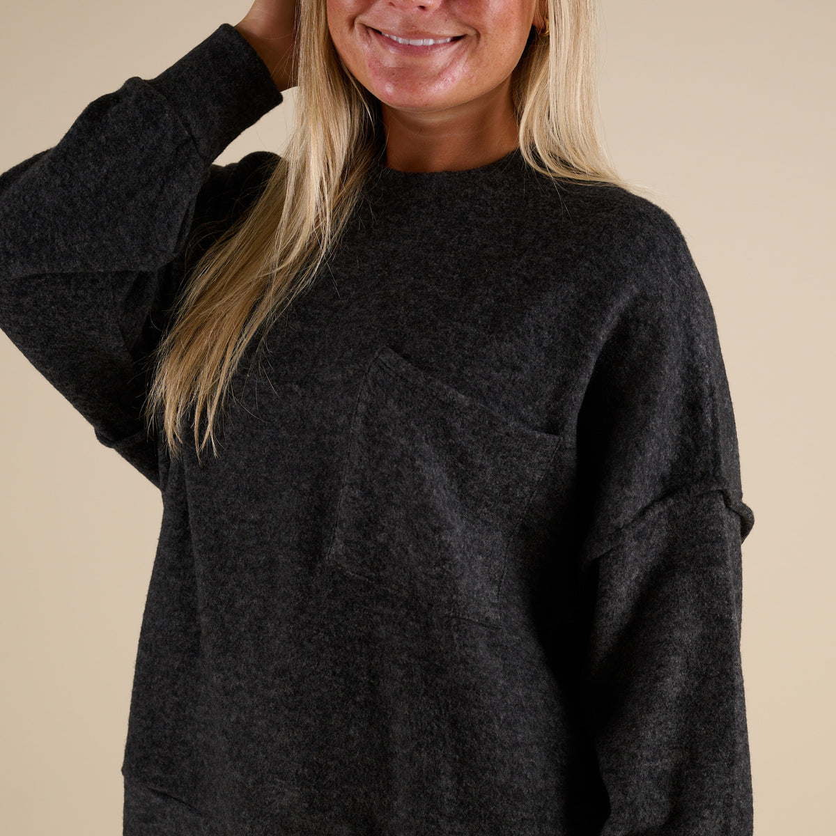 Person wearing a dark gray sweater against a beige background