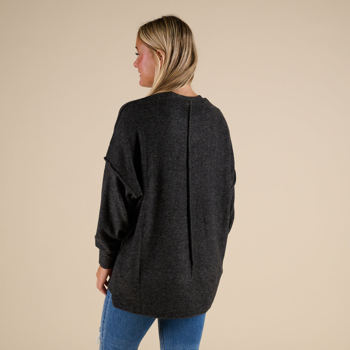 Person wearing a dark gray sweater and blue jeans on a beige background