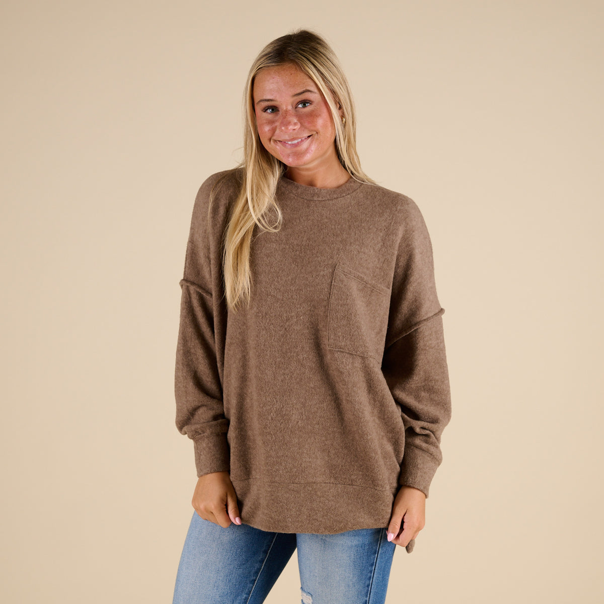 Woman wearing a brown sweater and blue jeans against a beige background