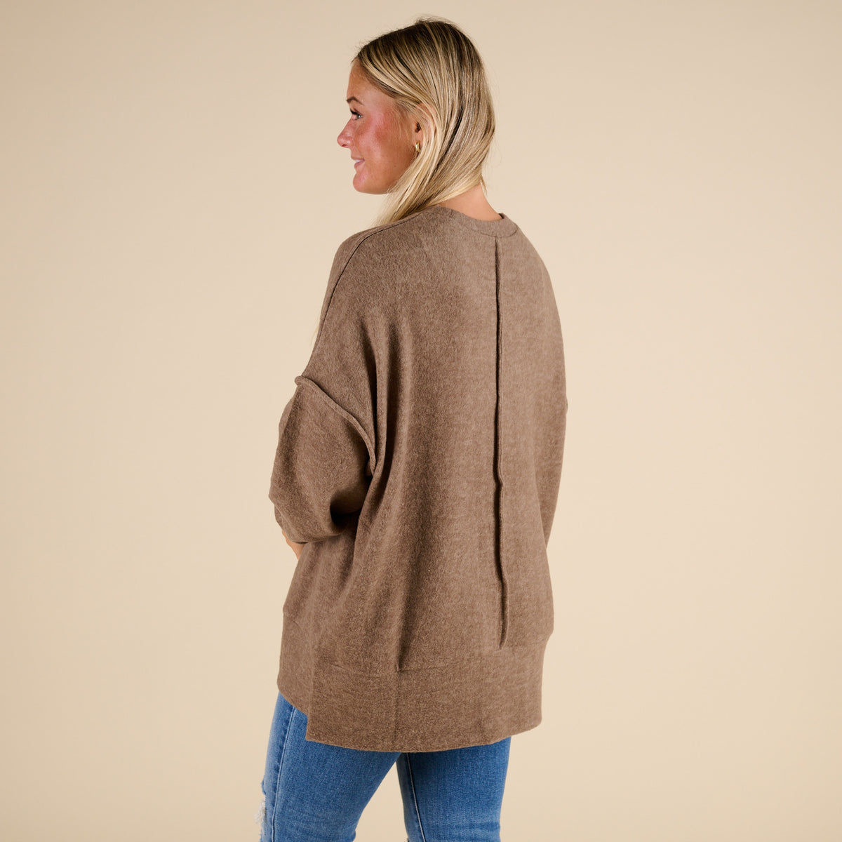 Woman wearing a brown cardigan and blue jeans on a beige background
