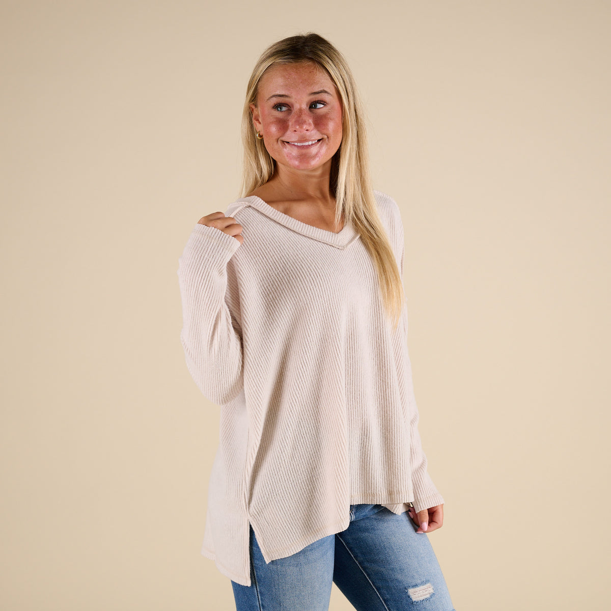 Woman wearing a beige sweater and blue jeans against a beige background