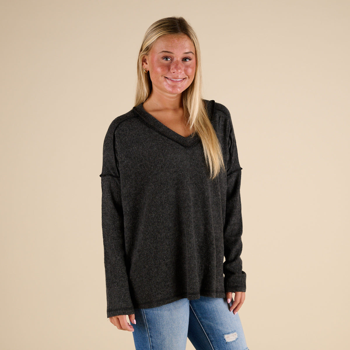 Woman wearing a dark gray hoodie and jeans on a beige background