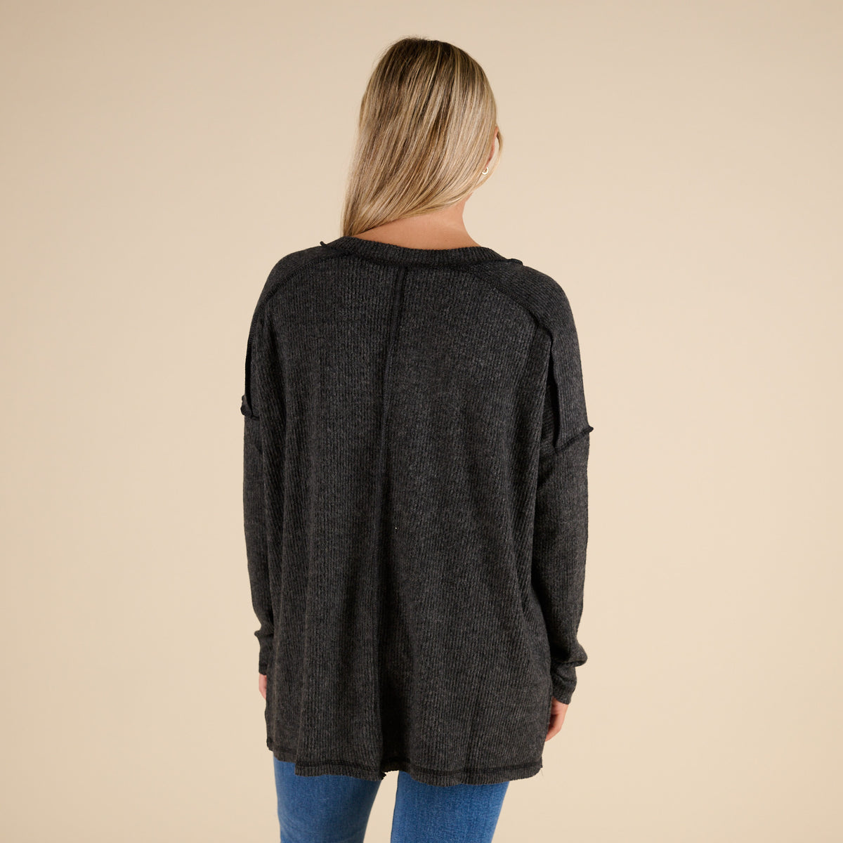 Person wearing a dark gray cardigan on a beige background