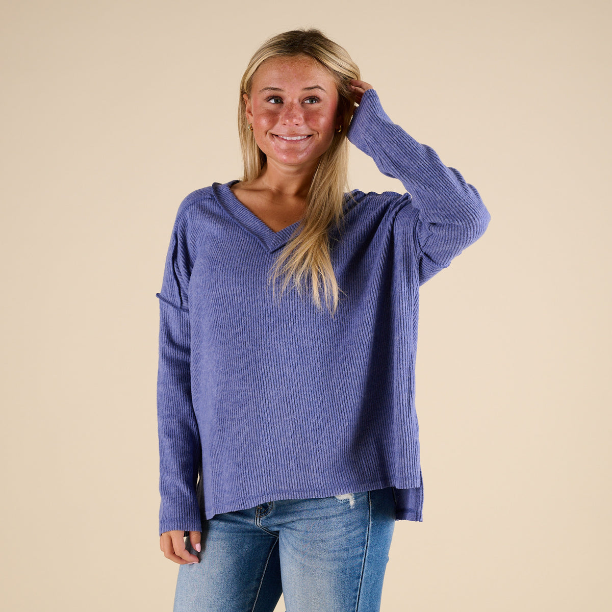 Woman wearing a blue sweater and jeans against a beige background
