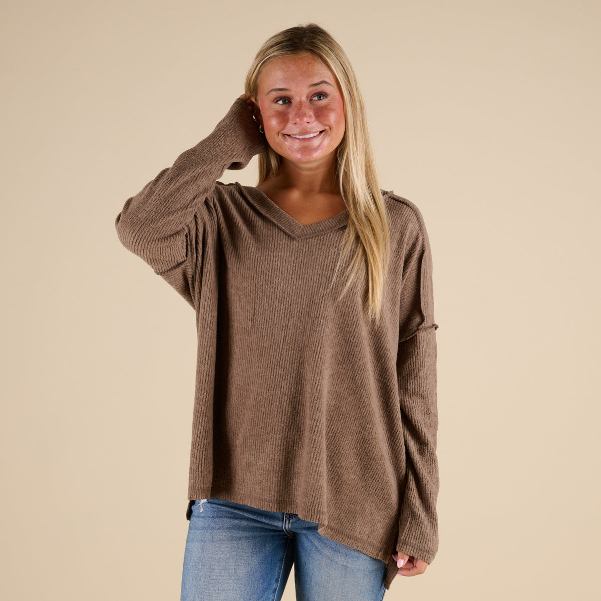 Woman wearing a brown sweater and blue jeans against a beige background