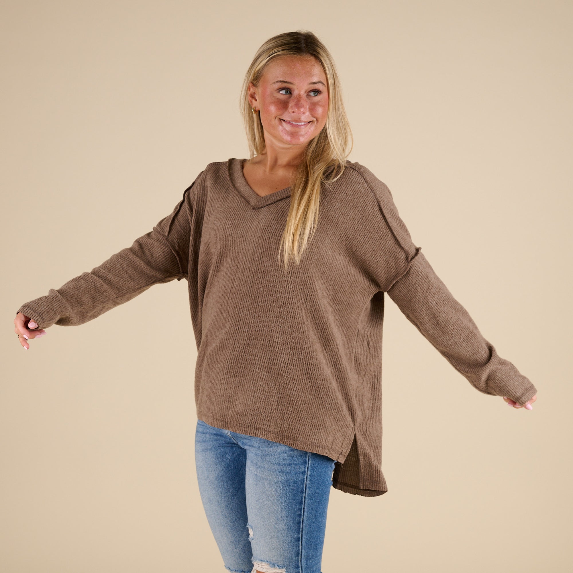 Woman wearing a brown sweater and blue jeans on a beige background