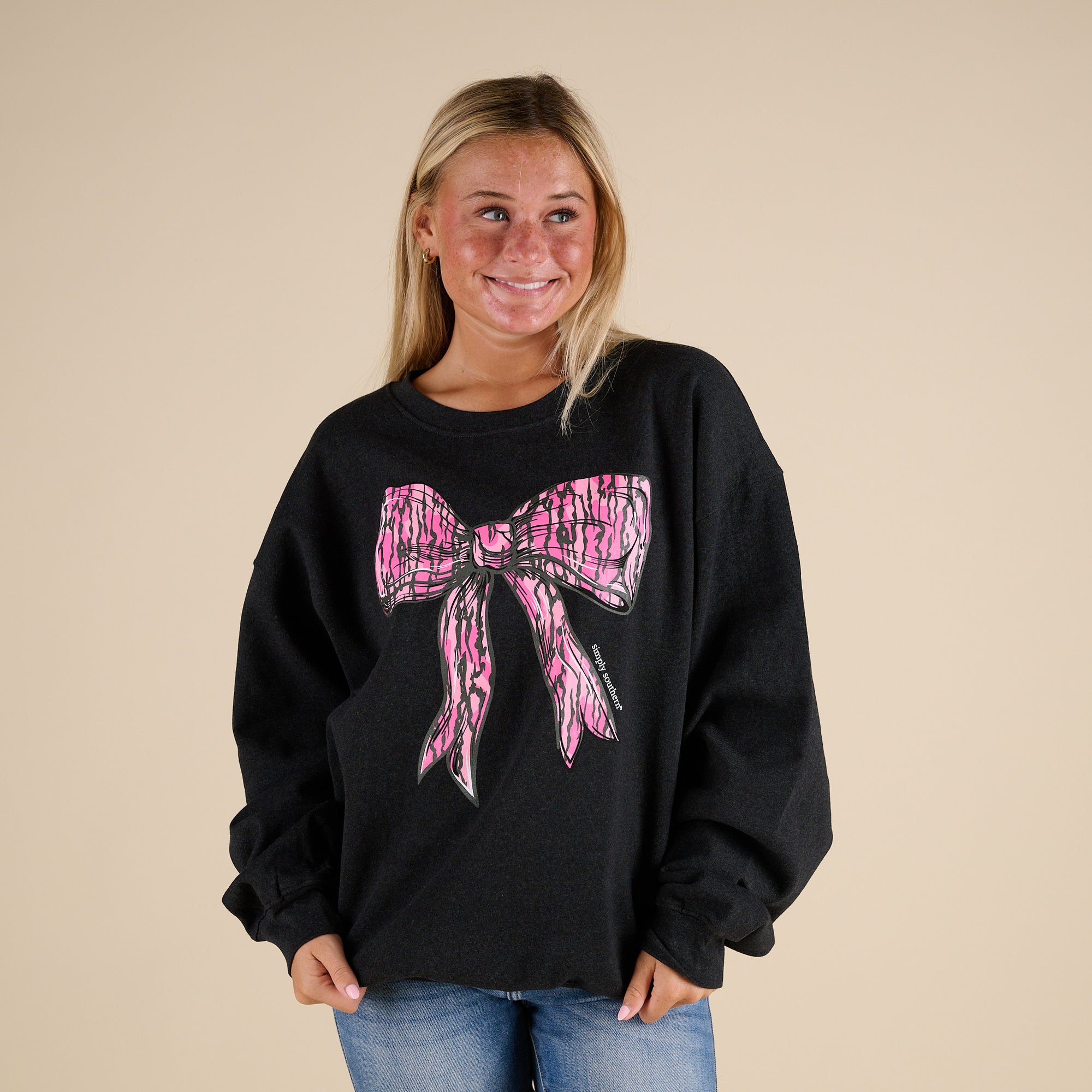 Model Wearing a black simply southern sweatshirt with large pink camo bow on the front.
