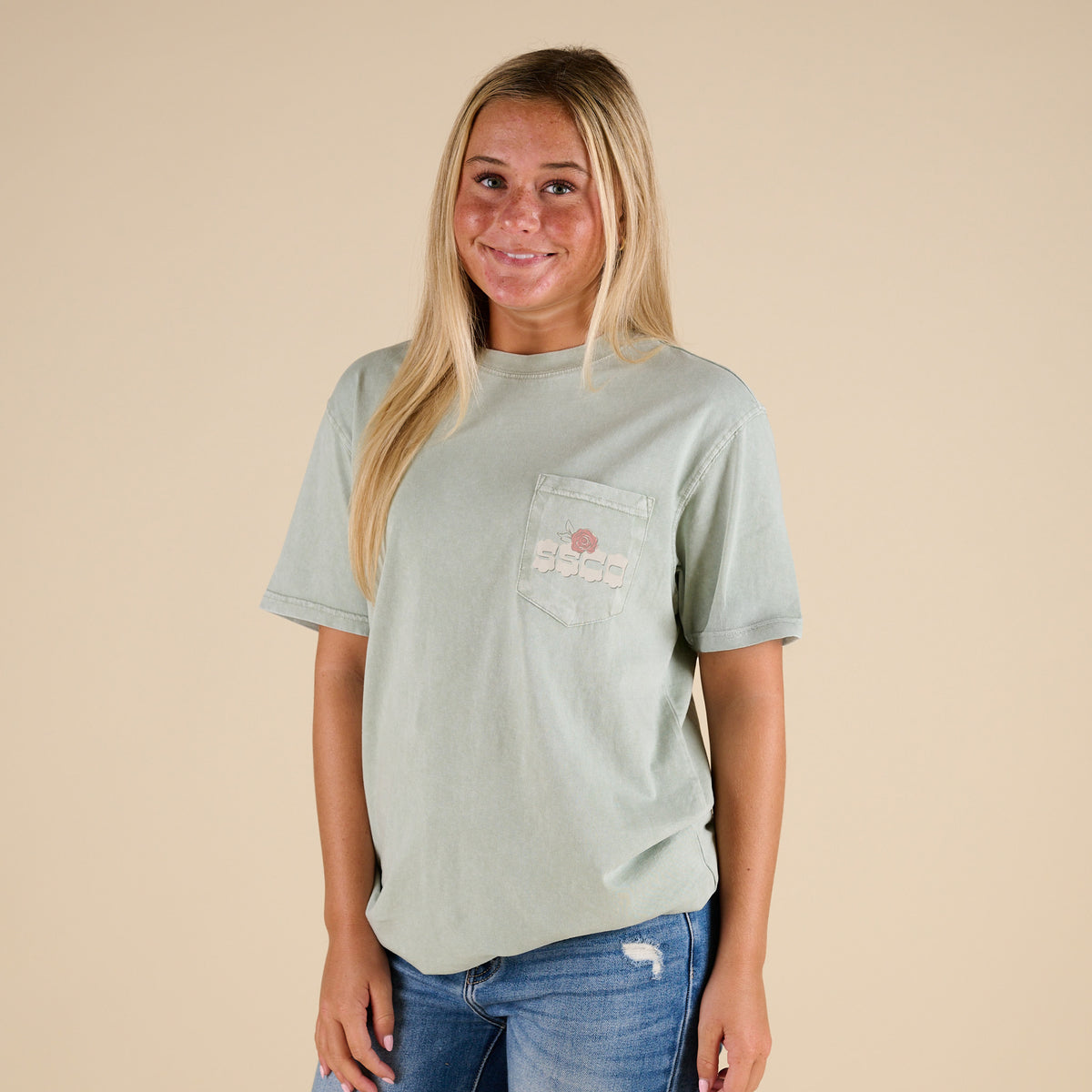 Woman wearing a light green t-shirt with a logo on a beige background
