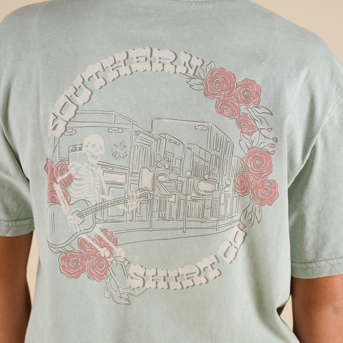Light green t-shirt with a graphic design of a person playing guitar and roses on the back.