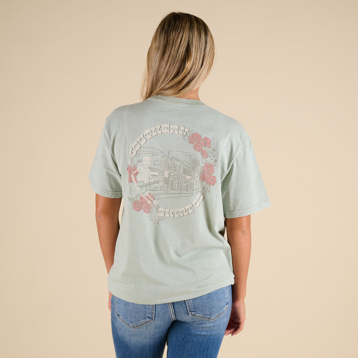 Person wearing a light green t-shirt with a graphic design on the back, standing against a beige background.