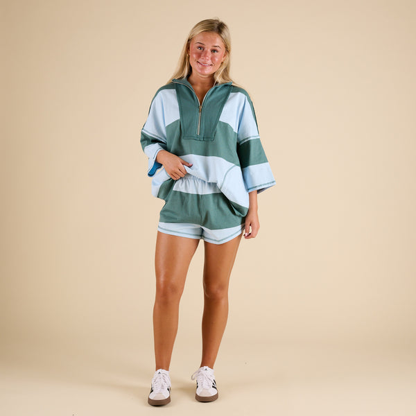 Model wearing FP Movement Retro Rugby Set in Heritage Green Combo, featuring an oversized half-zip striped top with pockets and matching striped shorts.