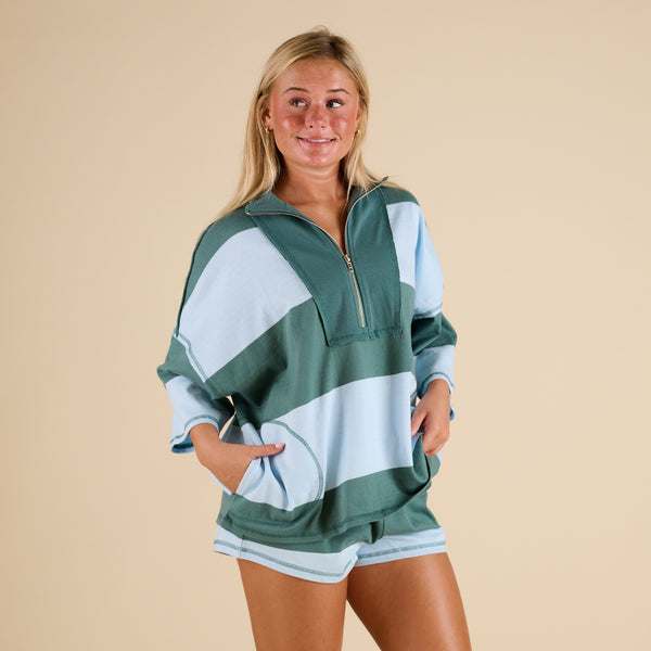 Model wearing FP Movement Retro Rugby Set in Heritage Green Combo, featuring an oversized half-zip striped top with pockets and matching striped shorts.