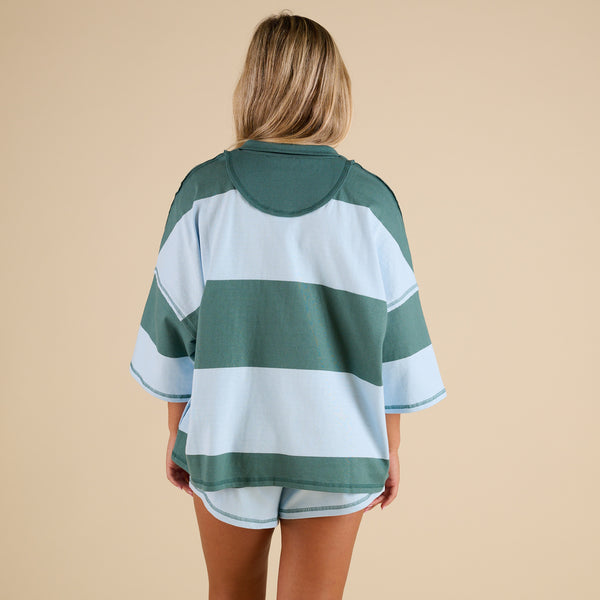 Model wearing FP Movement Retro Rugby Set in Heritage Green Combo, featuring an oversized half-zip striped top with pockets and matching striped shorts.