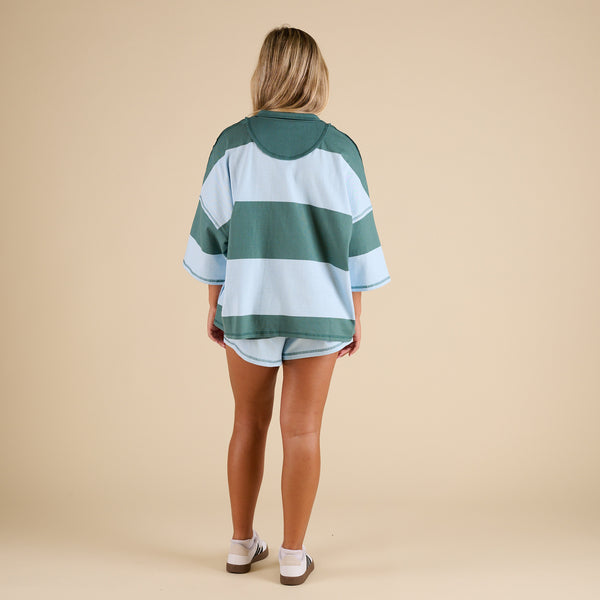 Model wearing FP Movement Retro Rugby Set in Heritage Green Combo, featuring an oversized half-zip striped top with pockets and matching striped shorts.