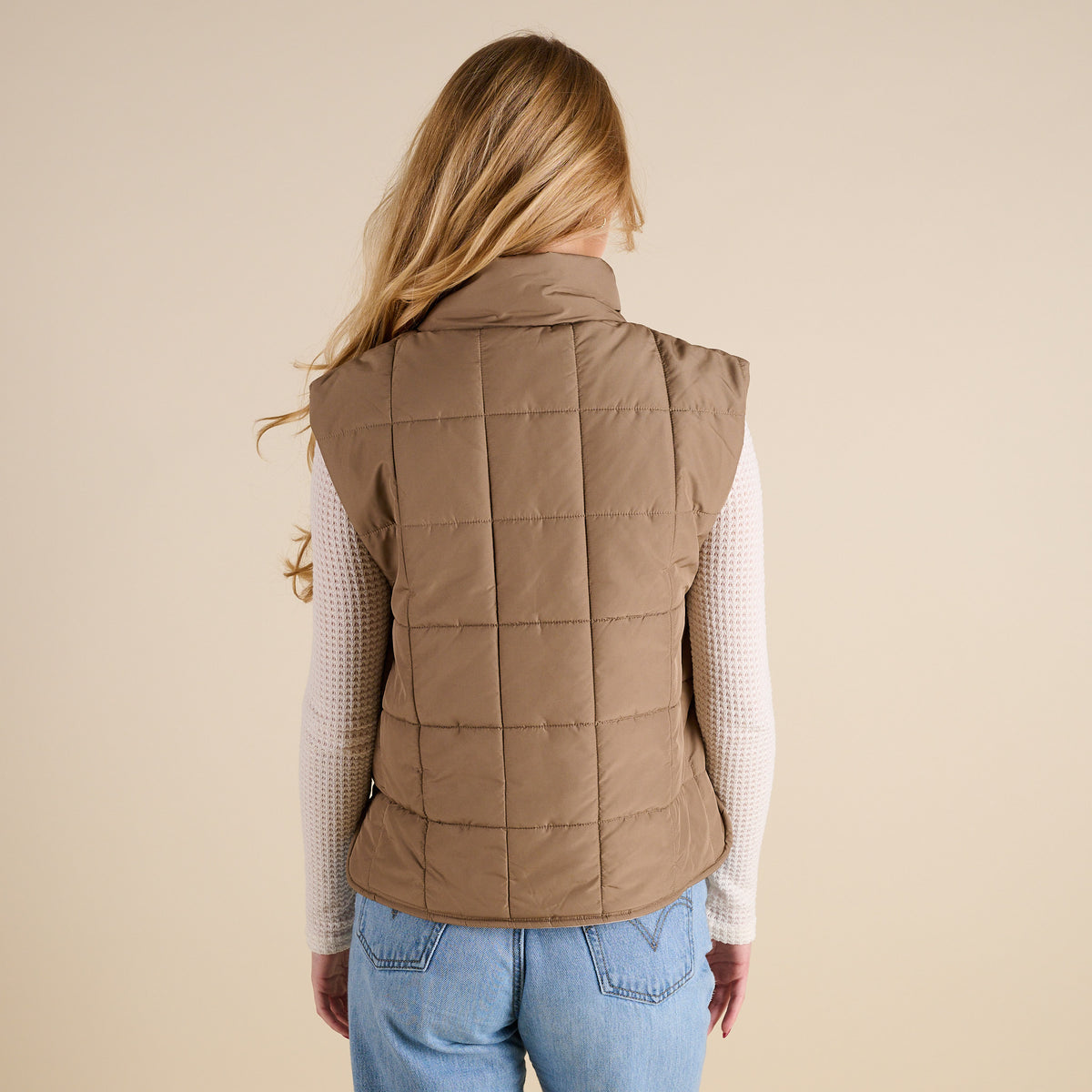 Person wearing a brown quilted vest on a beige background