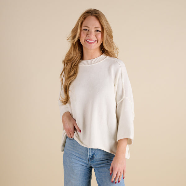 Women’s ivory knit mockneck sweater with relaxed silhouette, ribbed neckline, and three-quarter sleeves, shown from the front paired with light wash jeans.