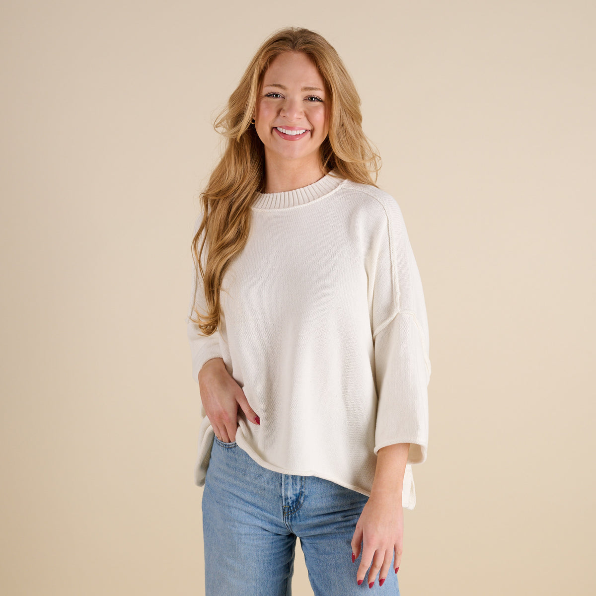 Women’s ivory knit mockneck sweater with relaxed silhouette, ribbed neckline, and three-quarter sleeves, shown from the front paired with light wash jeans.