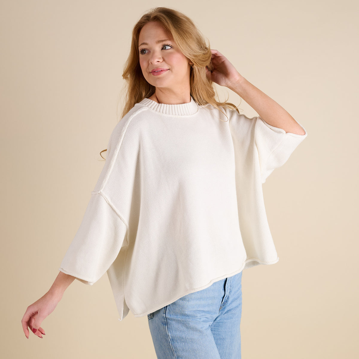 Women’s ivory knit mockneck sweater with loose fit, drop shoulders, and three-quarter sleeves, shown in angled view highlighting drape and textured knit fabric.