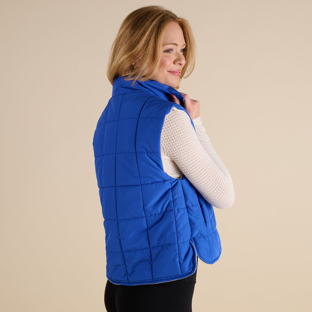Woman wearing a blue puffer vest on a beige background