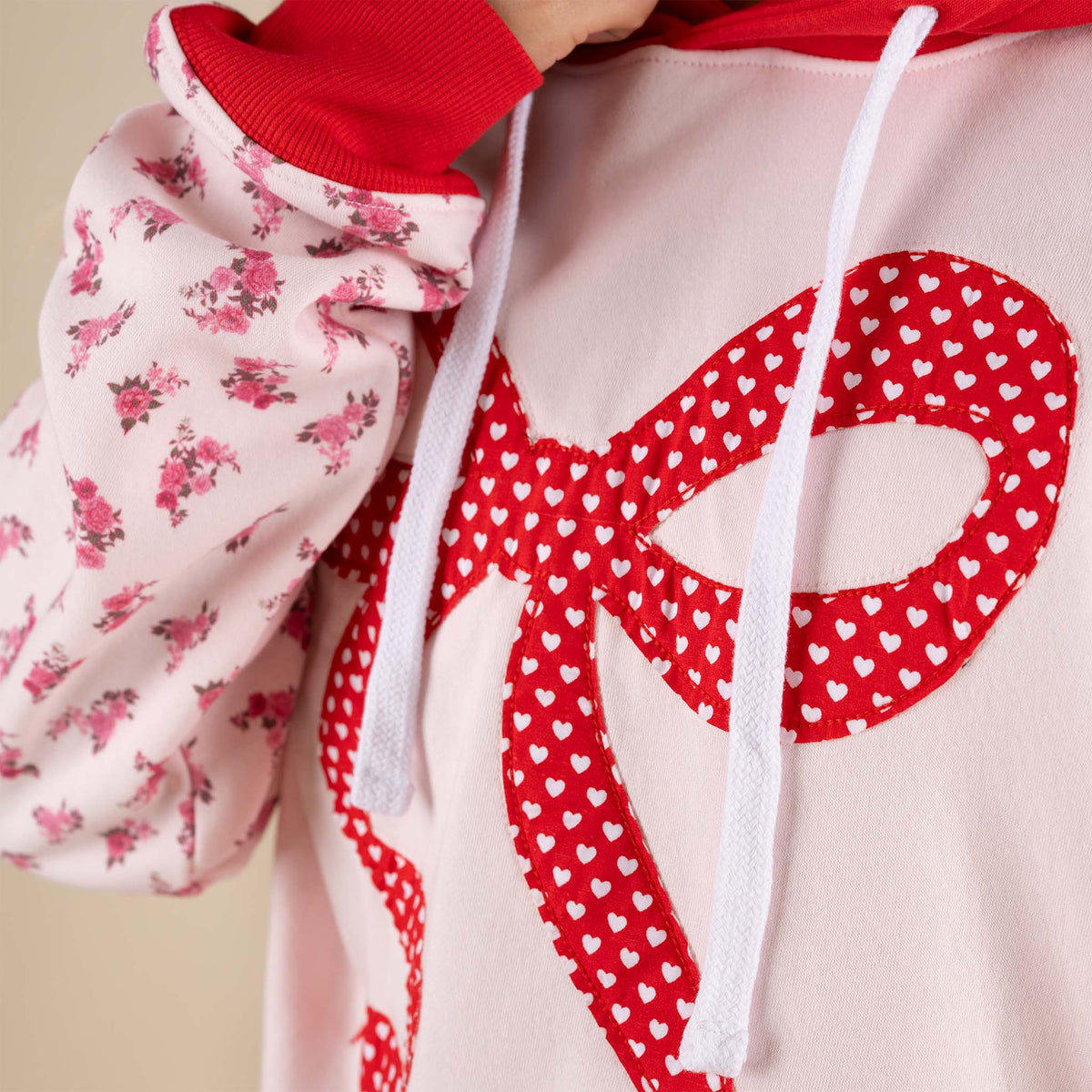 Simply Southern Bow Love Hoodie in Light Pink with contrasting red hood and hem, and floral sleeves.