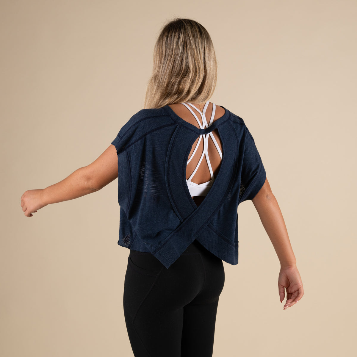 Woman wearing a navy blue activewear top with a cutout back and black leggings.